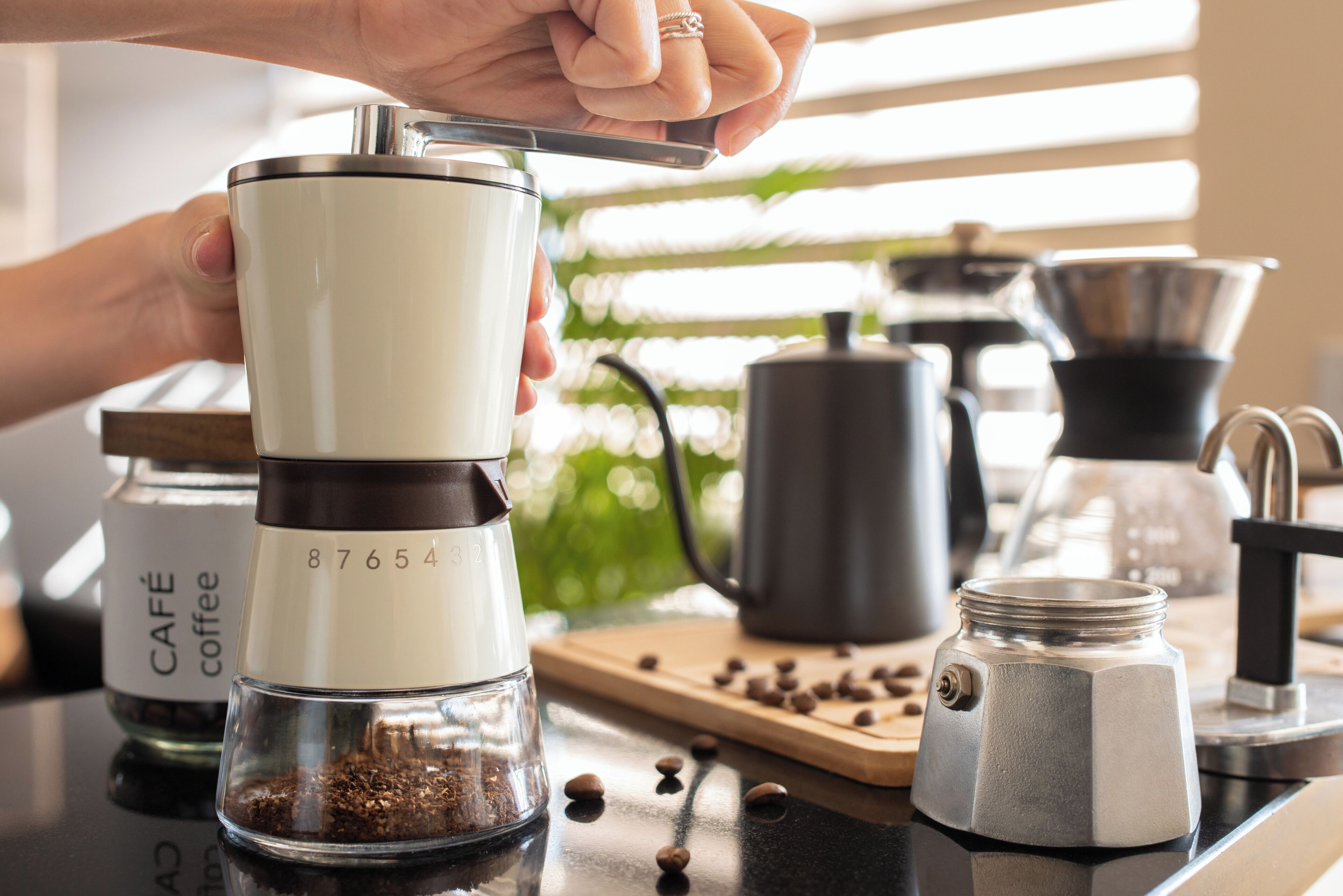 A coffee maker with a clear glass container, a coffee grinder, and a jar labeled "CAFE coffee" on a kitchen counter.
