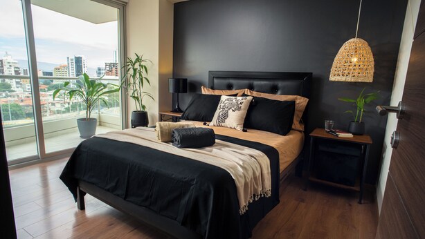 Un dormitorio moderno con una cama grande, vista a la ciudad y una lámpara colgante.