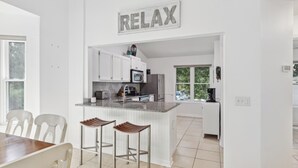Una cocina moderna con muebles blancos, una isla central con taburetes y un cartel con la palabra 'RELAX'.