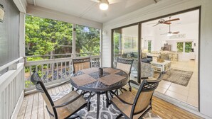 Un patio cubierto con una mesa redonda y sillas, ventanas amplias y vista al jardín trasero.