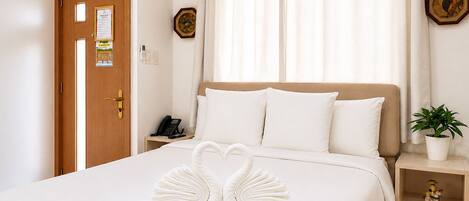 A hotel room with a bed, a wooden door, a bedside table with a phone, a potted plant, and a decorative item on the nightstand.