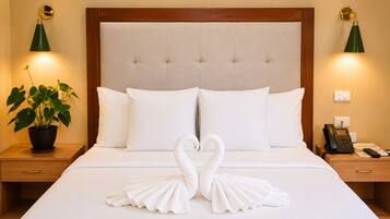 A hotel room with a large bed, two bedside tables, a potted plant, and a swan-shaped decoration on the bed.