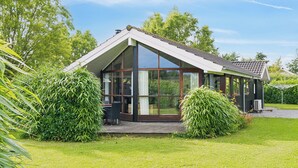 A modern house with a large glass front, a wooden deck, and a sloped roof. - Well-equipped summer house near Skovmose (Sydals)