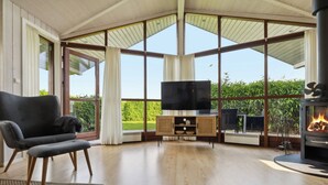 A room with a large window, a television, a fireplace, and a chair. - Well-equipped summer house near Skovmose (Sydals)
