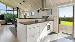 A modern kitchen with a large island, stainless steel range hood, and a sliding glass door leading to a deck. - Well-equipped summer house near Skovmose (Sydals)