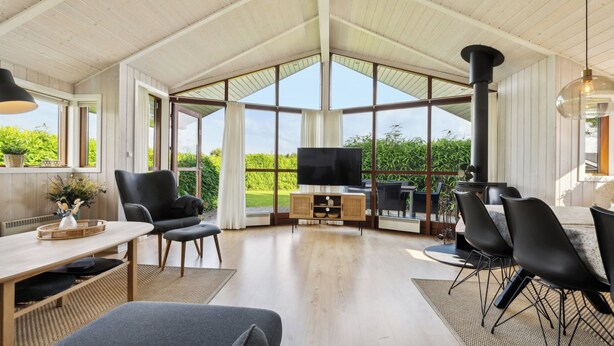A spacious room with a high ceiling, large windows, a dining area, and a television. - Well-equipped summer house near Skovmose (Sydals)