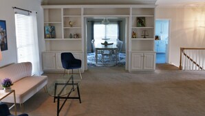 Un salon avec une table basse en verre, un fauteuil bleu, un canapé et un coin repas comprenant une table et des chaises.