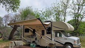 A Four Winds RV with a covered living area, a table with chairs, and a propane tank. - Cozy riverfront RV in the heart of wine country "Dandy @ Verde Retreat" (Cottonwood)