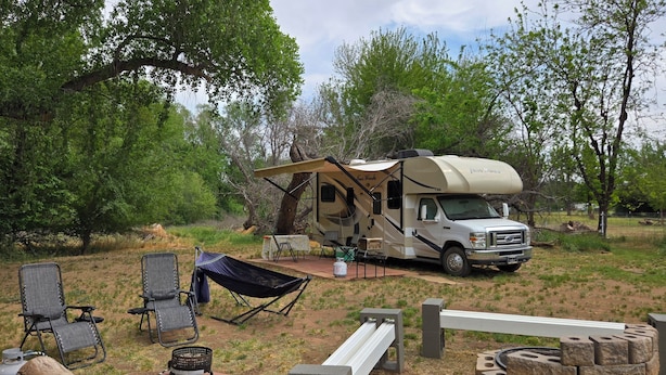 A recreational vehicle with a covered living area, surrounded by outdoor furniture and a fire pit. - Cozy riverfront RV in the heart of wine country "Dandy @ Verde Retreat" (Cottonwood)