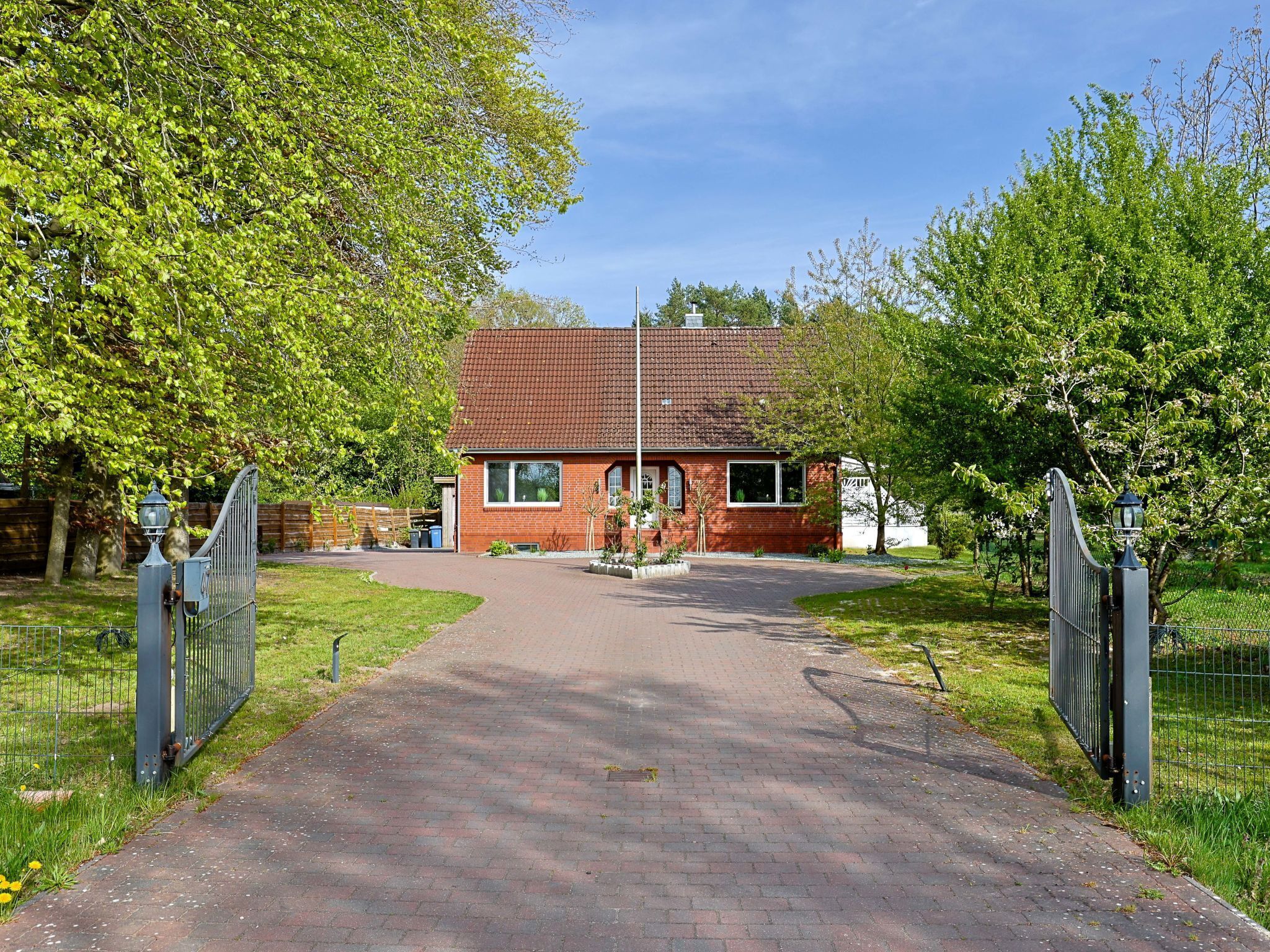 A brick house with a red-tiled roof, a paved driveway, and a metal gate.