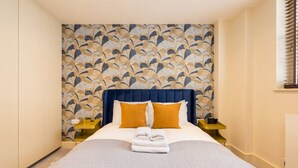 Ein Hotelzimmer mit einem großen Bett, zwei Nachttischen, einem blauen Kopfteil und einer gemusterten Tapete.