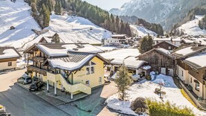 Un villaggio montano imbiancato dalla neve con edifici tradizionali in legno, una seggiovia e una vista chiara delle montagne circostanti.