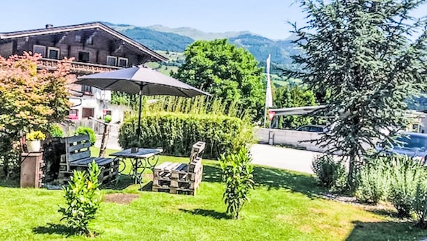 Un chalet con posti a sedere all'aperto, un tavolo e una sedia, immerso nel verde con montagne sullo sfondo.