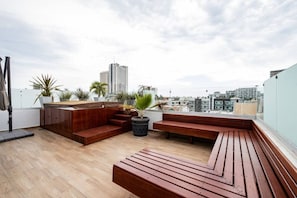 Une terrasse sur le toit, dotée de mobilier en bois, de plantes en pot et offrant une vue sur les bâtiments de la ville.