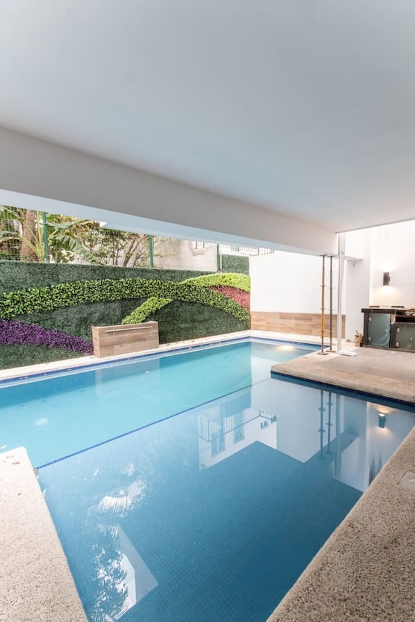 Une piscine à l’eau d’un bleu cristallin, entourée d’un jardin aménagé avec différentes espèces de plantes et d’une terrasse en bois.