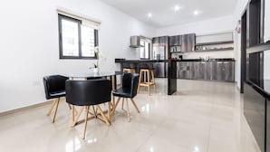 A modern kitchen with a dining area, featuring a round table with chairs, a window with blinds, and a built-in oven.