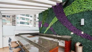 A modern kitchen with a green and purple vertical garden wall, a granite countertop, and a bar area with stools.