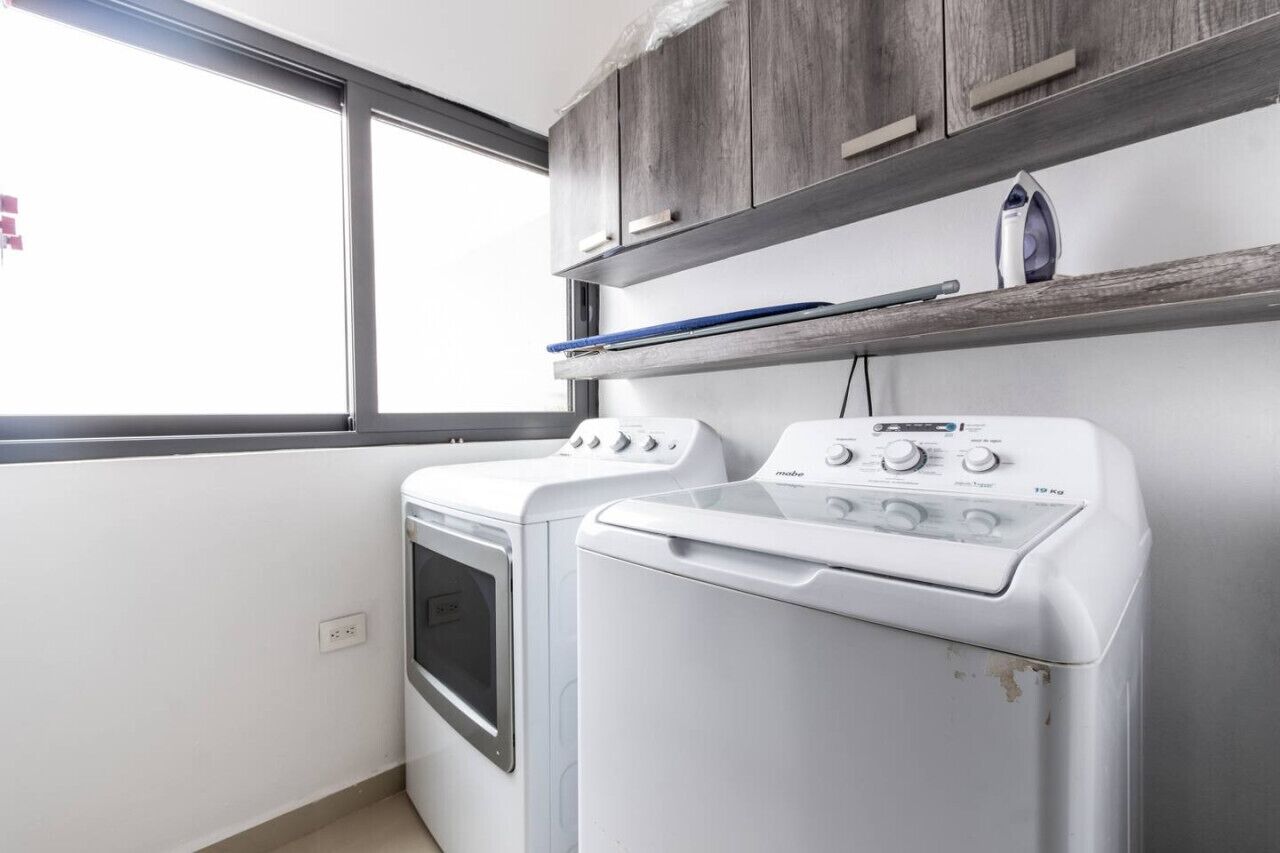 A laundry area with a washing machine and dryer, wooden cabinets, and a window.