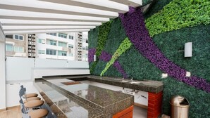 Eine moderne Küche mit einer senkrechten Wandgärtchen-Gestaltung in Grün und Violett, einer Arbeitsplatte aus Granit und einer Bar mit Hockern.