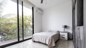 Ein modernes Schlafzimmer mit großem Fenster, einem Bett, einem Nachttisch und einem Kleiderschrank.