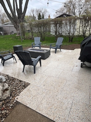 Eine Außenpatio-Terrasse mit einem Feuerkorb, zwei Adirondack-Stühlen und einem Grill.