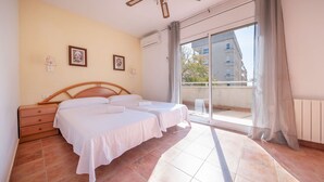 A bedroom with two beds, a wooden headboard, a small bedside table, and a window with a view of buildings and trees. - R141 - C6 Manila Resort Patio (Calafell)