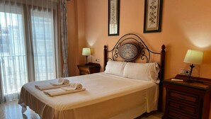 A neatly made bed with towels, a headboard with a decorative plate, two bedside tables with lamps, and framed floral artwork on the walls. - Cervantes in Javea X bia (Javea)