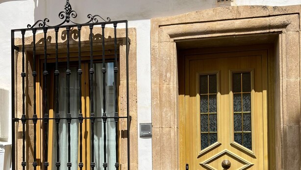 A building with a number 29 sign, a wooden door with a diamond pattern, and a barred window. - Cervantes in Javea X bia (Javea)