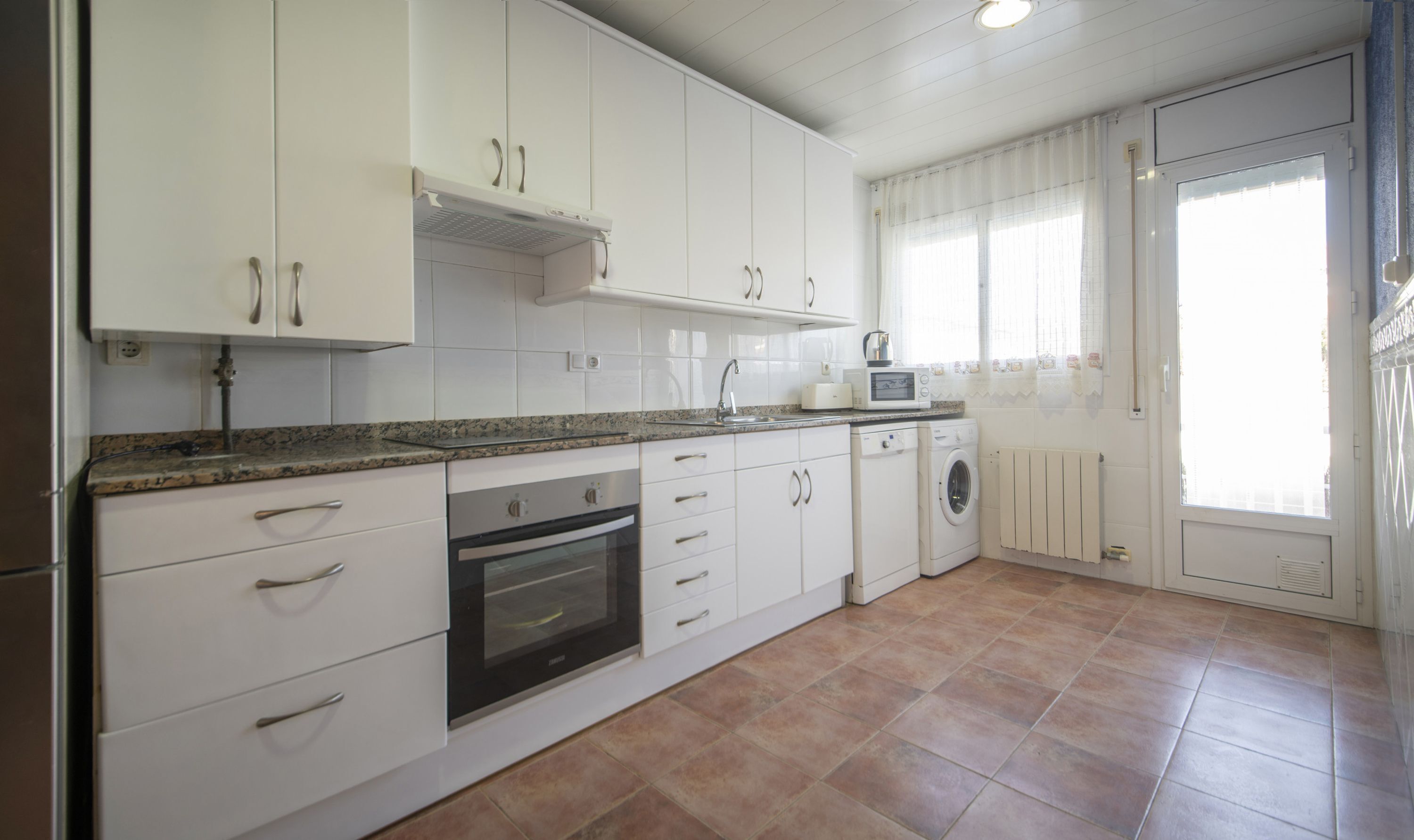 Une cuisine avec des meubles blancs, un four encastré, un four à micro-ondes et un lave-linge.