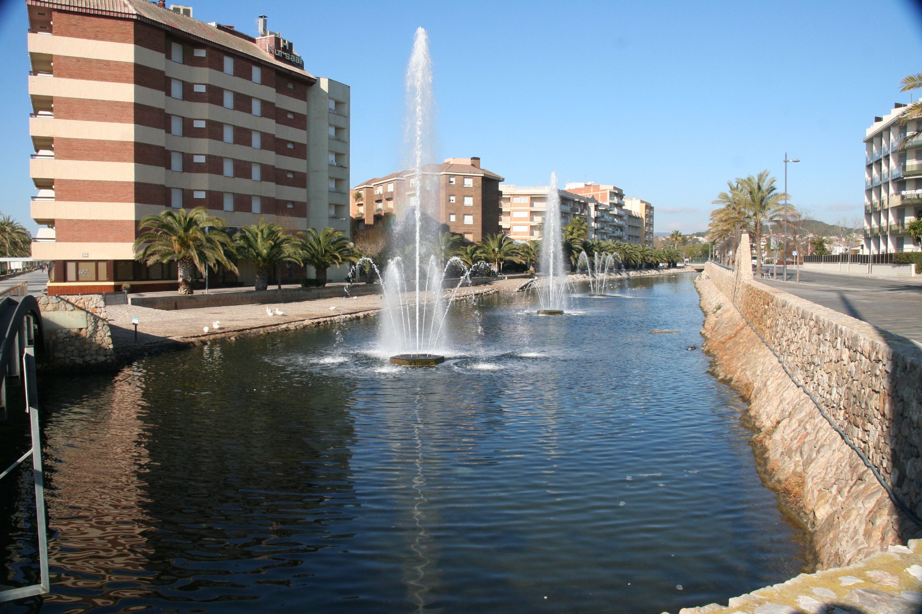 Ein Kanal mit Springbrunnen, umgeben von Gebäuden und Palmen.