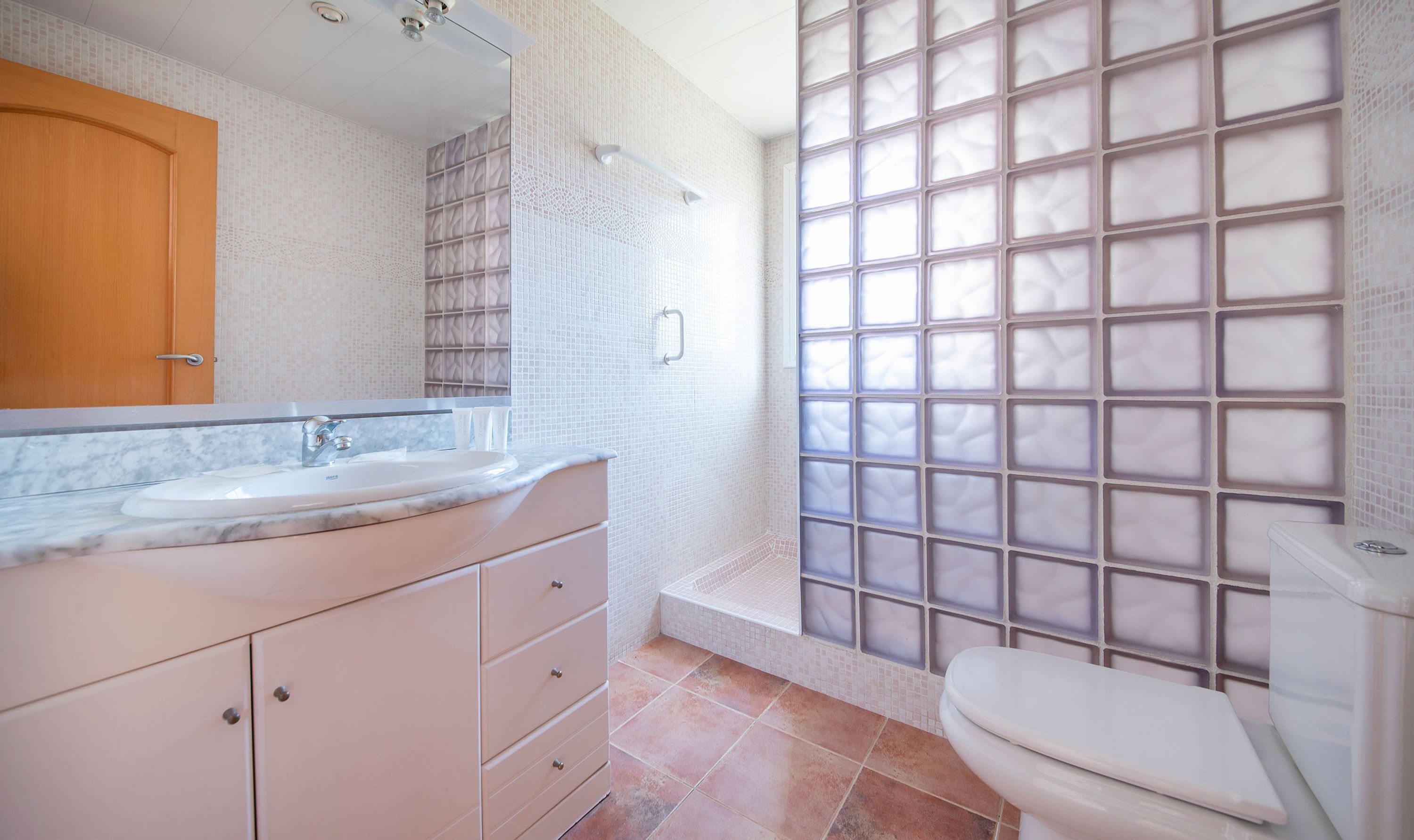 Ein Badezimmer mit Marmorwaschbecken, Holztür, gefliestem Duschbereich und Toilette.