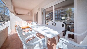 Ein Balkon mit weißem Tisch und Stühlen, einem Fliesenboden und Blick auf Gebäude durch große Fenster.
