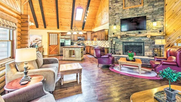 A log cabin interior with a stone fireplace, wooden ceiling beams, and a cozy living area with furniture. - Rustic Pinetop Log Cabin w/ Fire Pit + Grill! (Pinetop)