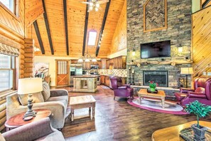 A log cabin interior with a stone fireplace, wooden ceiling beams, and a cozy living area with furniture. - Rustic Pinetop Log Cabin w/ Fire Pit + Grill! (Pinetop)