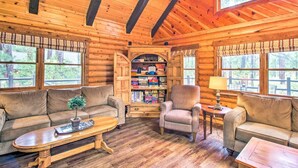 A log cabin interior with a wooden ceiling, two sofas, a coffee table, a lamp, and a bookshelf. - Rustic Pinetop Log Cabin w/ Fire Pit + Grill! (Pinetop)