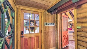 A wooden interior with a glass door, a coat rack, and a red door leading to another room. - Rustic Pinetop Log Cabin w/ Fire Pit + Grill! (Pinetop)