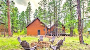 A cabin with a fire pit and four Adirondack chairs in a forest setting. - Rustic Pinetop Log Cabin w/ Fire Pit + Grill! (Pinetop)