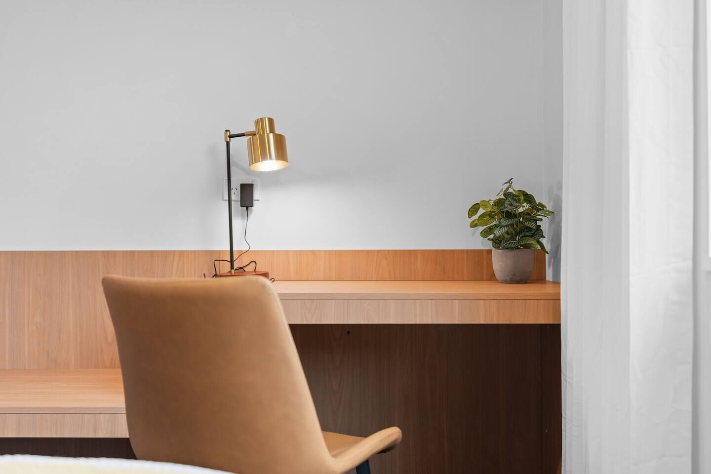 Un espace de travail moderne avec un bureau en bois, une chaise marron, une lampe de bureau dorée et une plante en pot.