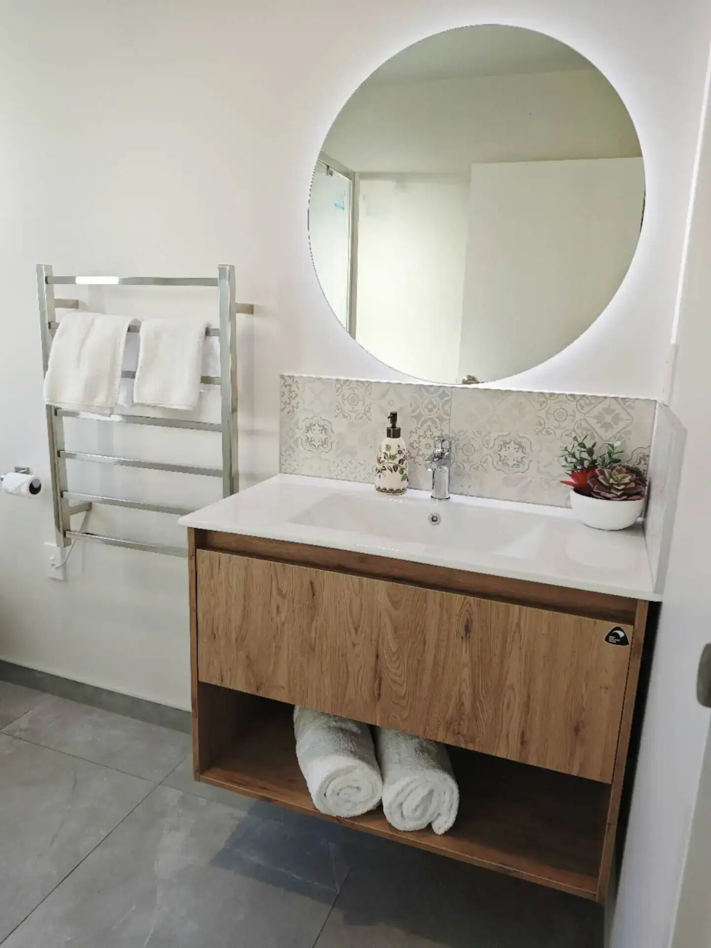 Une salle de bain avec un meuble-lavabo en bois, un miroir rond et un porte-serviettes.