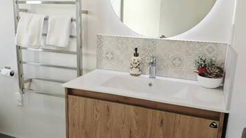 Une salle de bain avec un meuble-lavabo en bois, un miroir rond et un porte-serviettes.