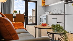 Ein modernes Hotelzimmer mit Sofa, Esstisch und Küchenzeile, inklusive Waschmaschine.