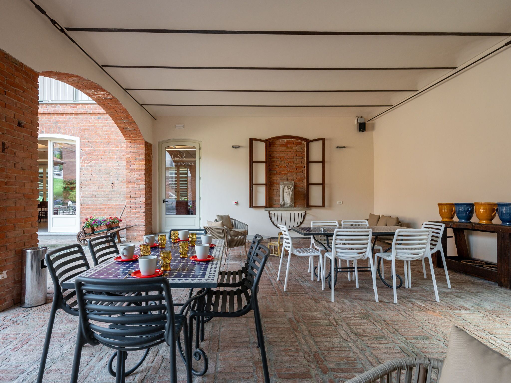 An outdoor dining area with brick walls, a glass door entrance, and a mix of metal and white chairs.