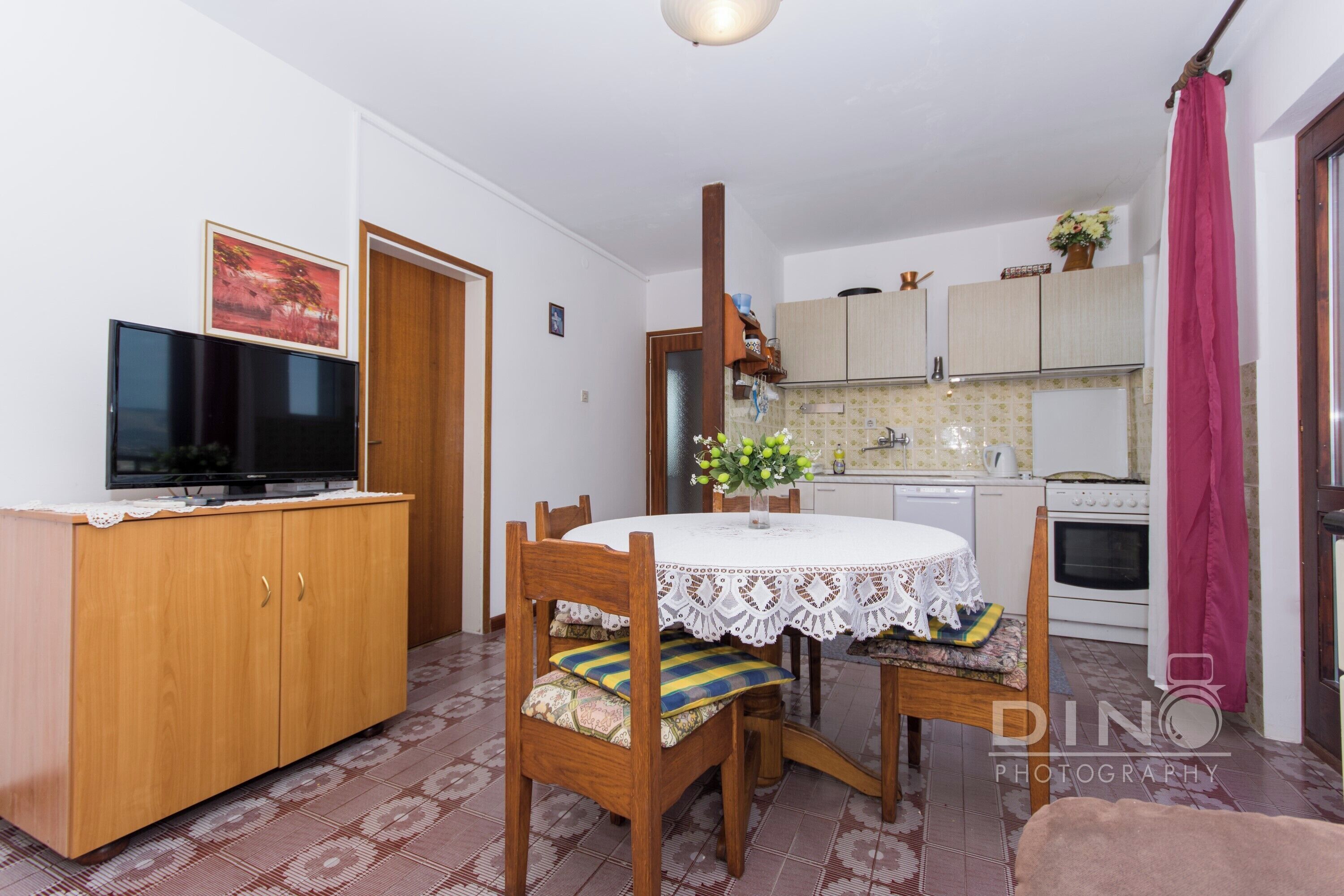 A compact living space with a dining area, kitchenette, and a television on a wooden cabinet.