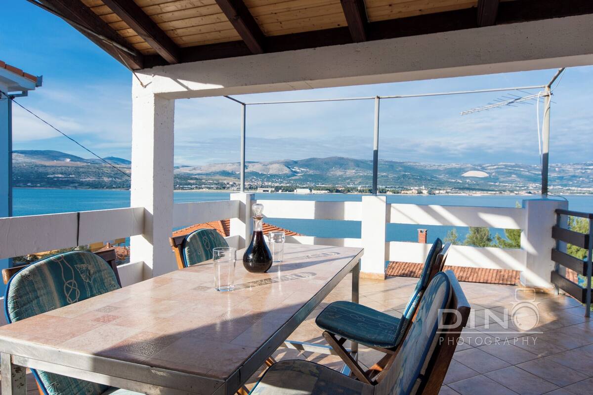 A terrace with a table and chairs, overlooking a scenic view of a body of water and distant mountains.