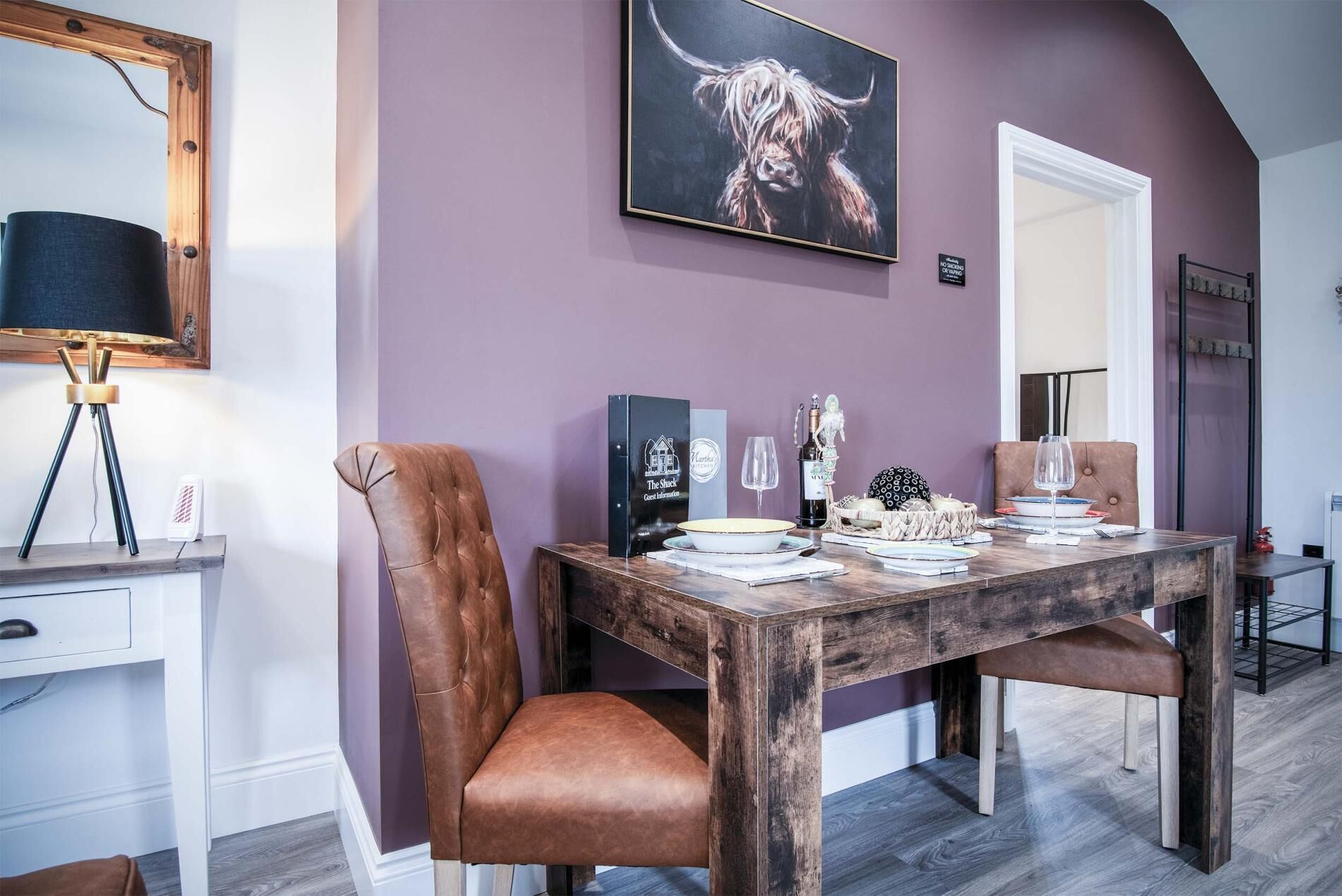 Un comedor con una mesa de madera, dos sillas de cuero marrón, un letrero negro con texto blanco y una obra de arte enmarcada en la pared.