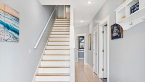 Una escalera con peldaños blancos y barandillas de madera que lleva a un rellano con un banco y un estante empotrado en la pared con objetos decorativos.