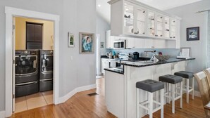 Una cocina moderna con electrodomésticos de acero inoxidable, armarios blancos y una isla central con taburetes de bar.