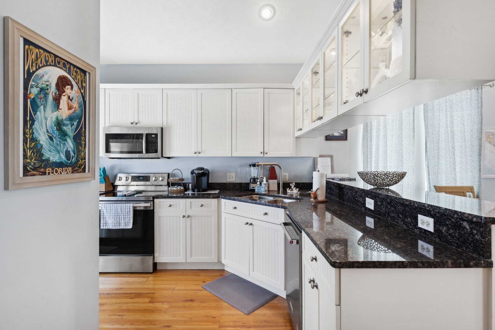 A modern kitchen with white cabinets, a granite countertop, stainless steel appliances, and a framed artwork on the wall.