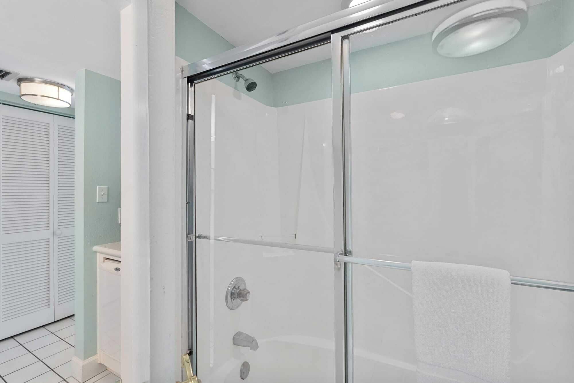 A modern bathroom with a glass-enclosed shower, a white towel hanging on the door, and a light green wall.