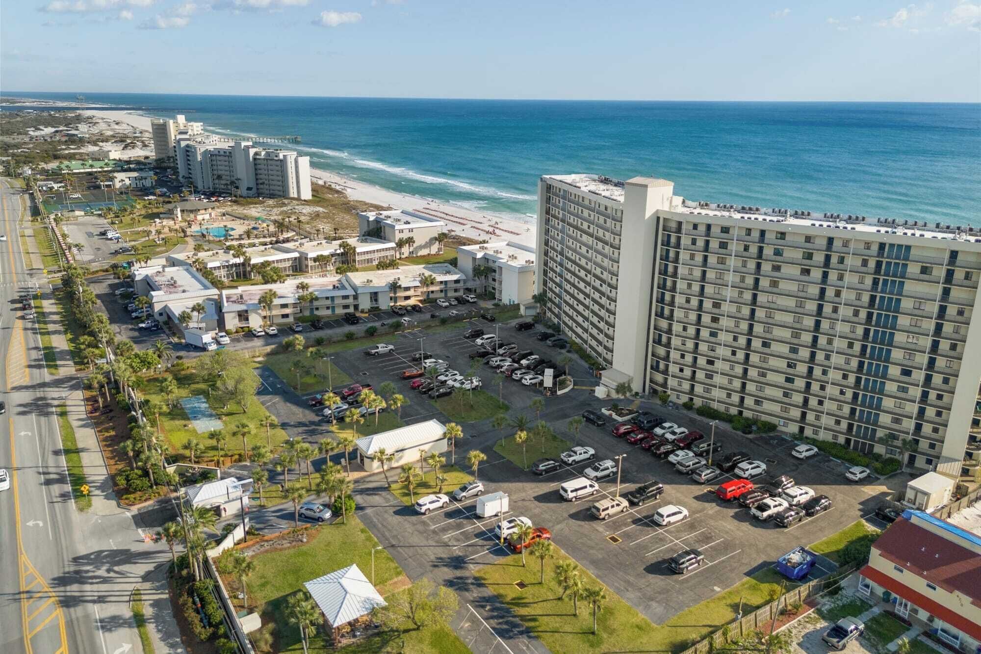 A coastal hotel with multiple parking lots, a beach view, and a large building with balconies.